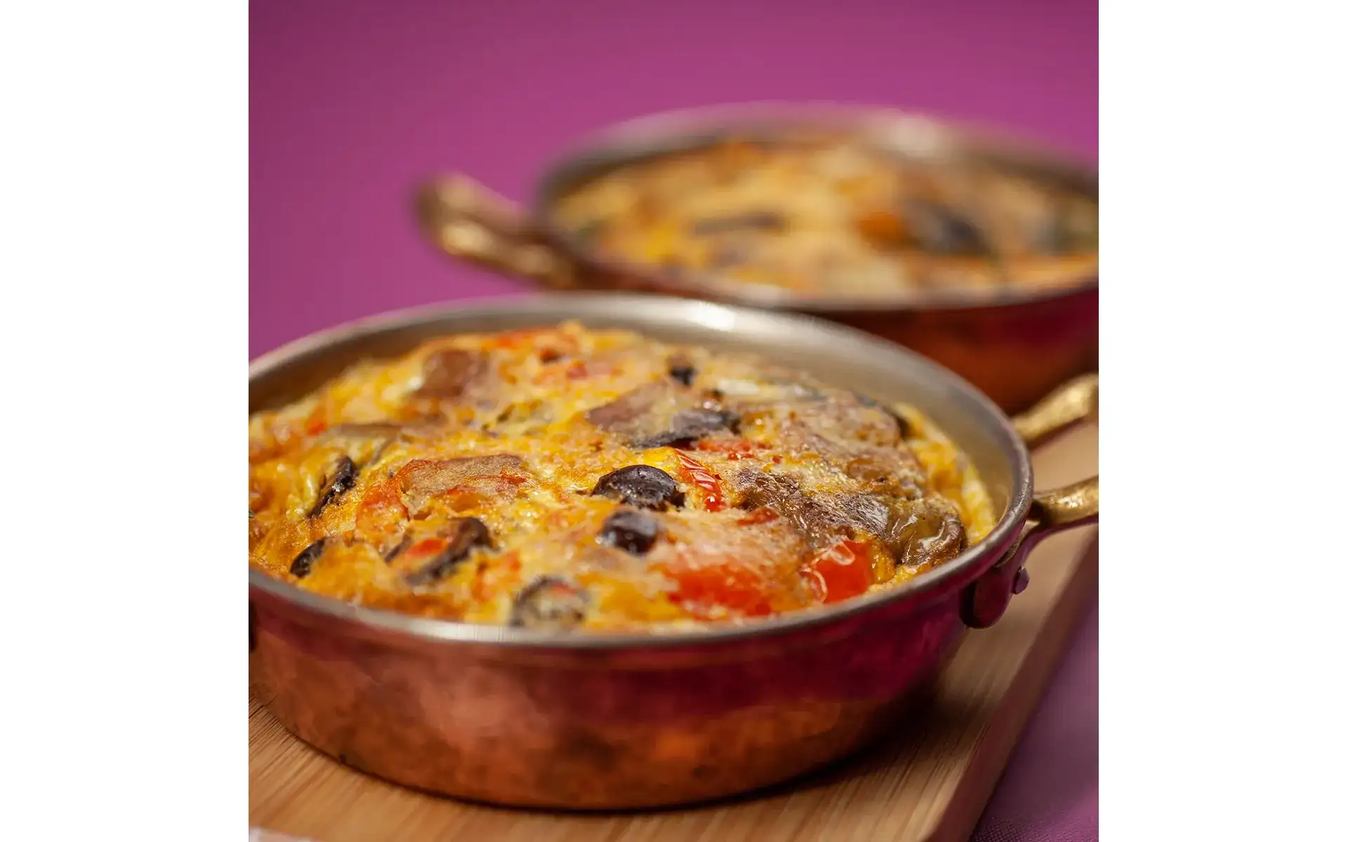 Due porzioni di frittata mediterranea, ricca di sapori e colori, su un tavolo di legno.