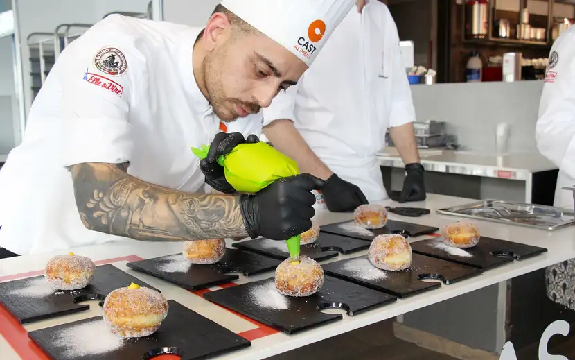 Chef Zuccheramelo (testimonial Orogel) prepara un piatto con maestria e guanti neri.